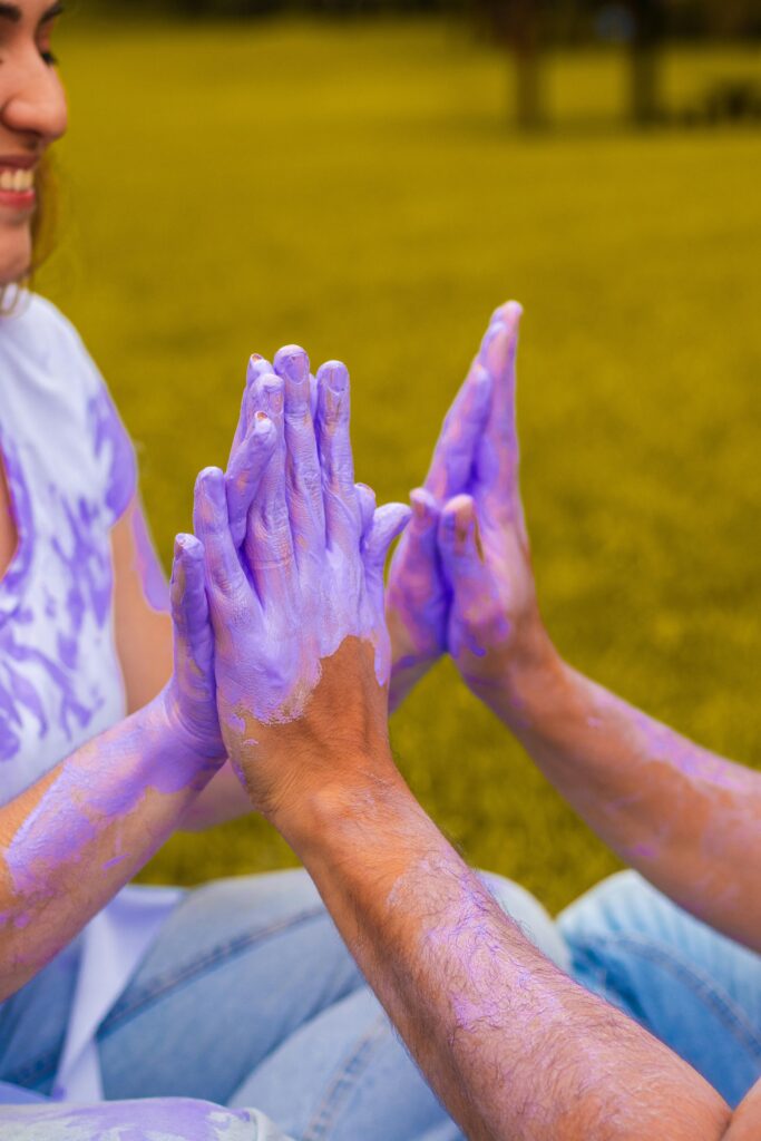 A happy couple enjoying a playful moment with their hands painted purple in an outdoor setting.